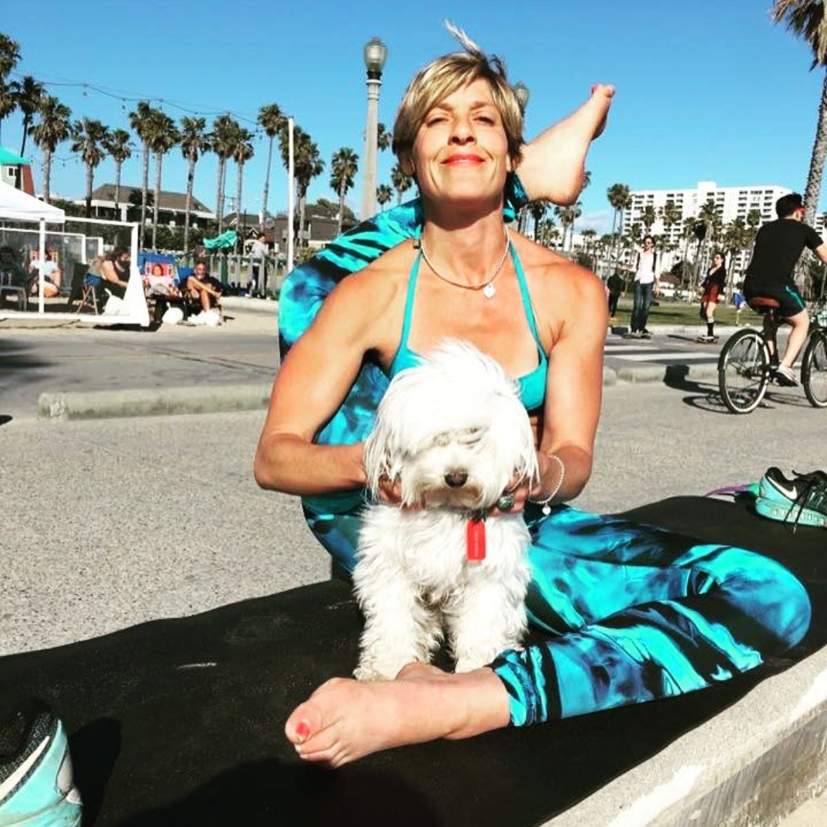 fluffy white dog held by a woman while she's doing yoga with one back leg over her neck