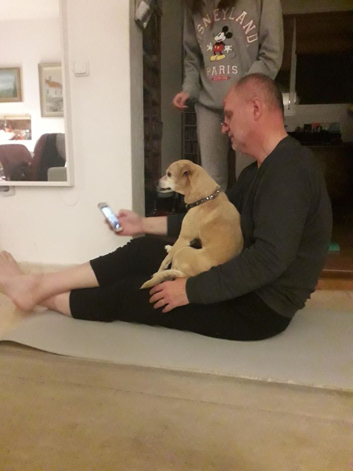 small brown dog being held on the lap of a man sitting on the floor