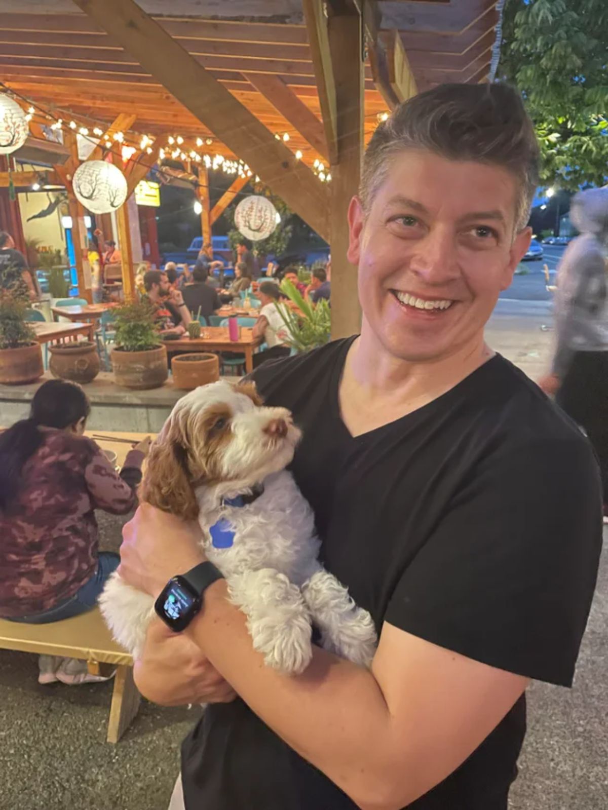 small fluffy brown and white puppy being carried by a man at a restaurant